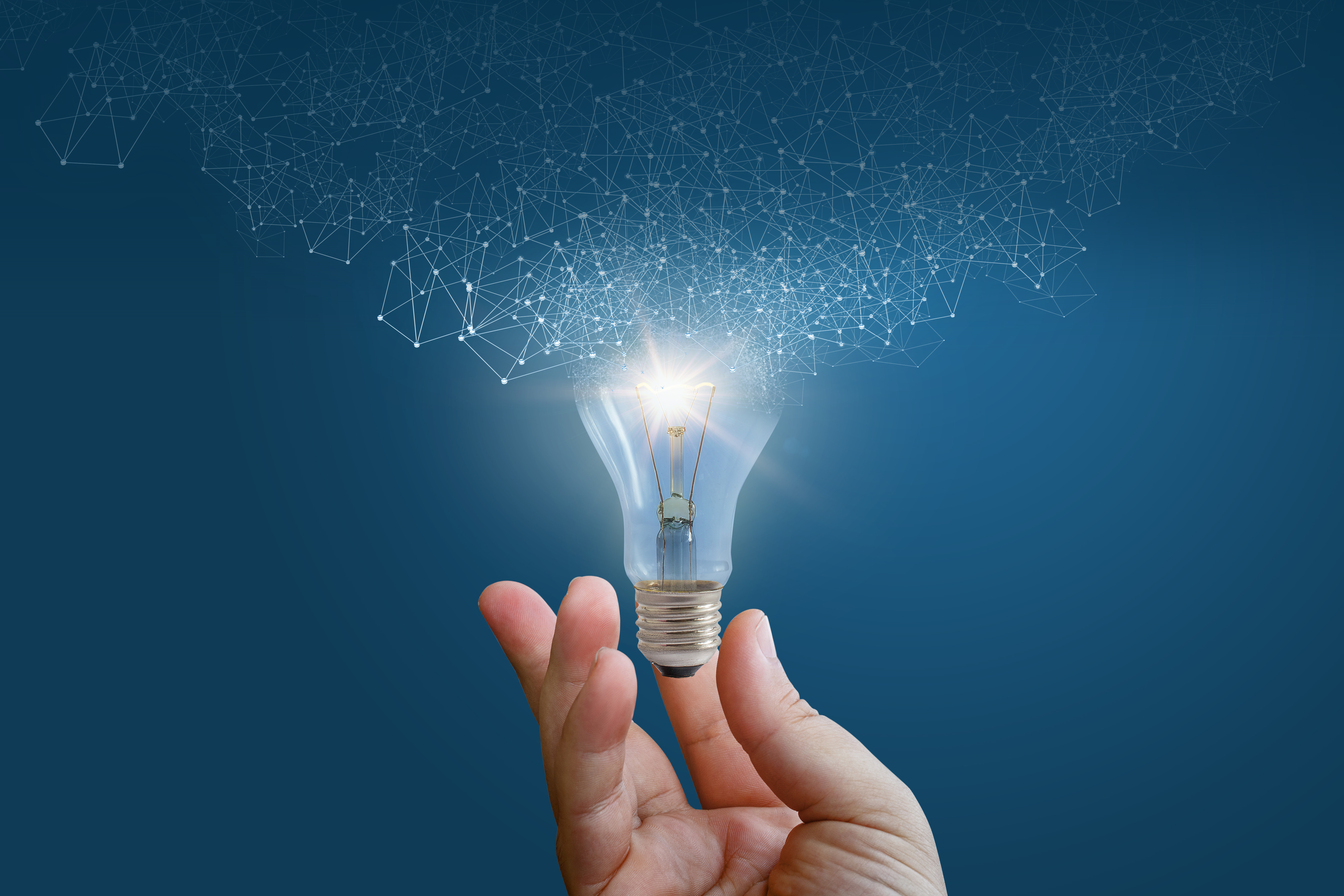 A hand holding a light bulb connected to a digital network