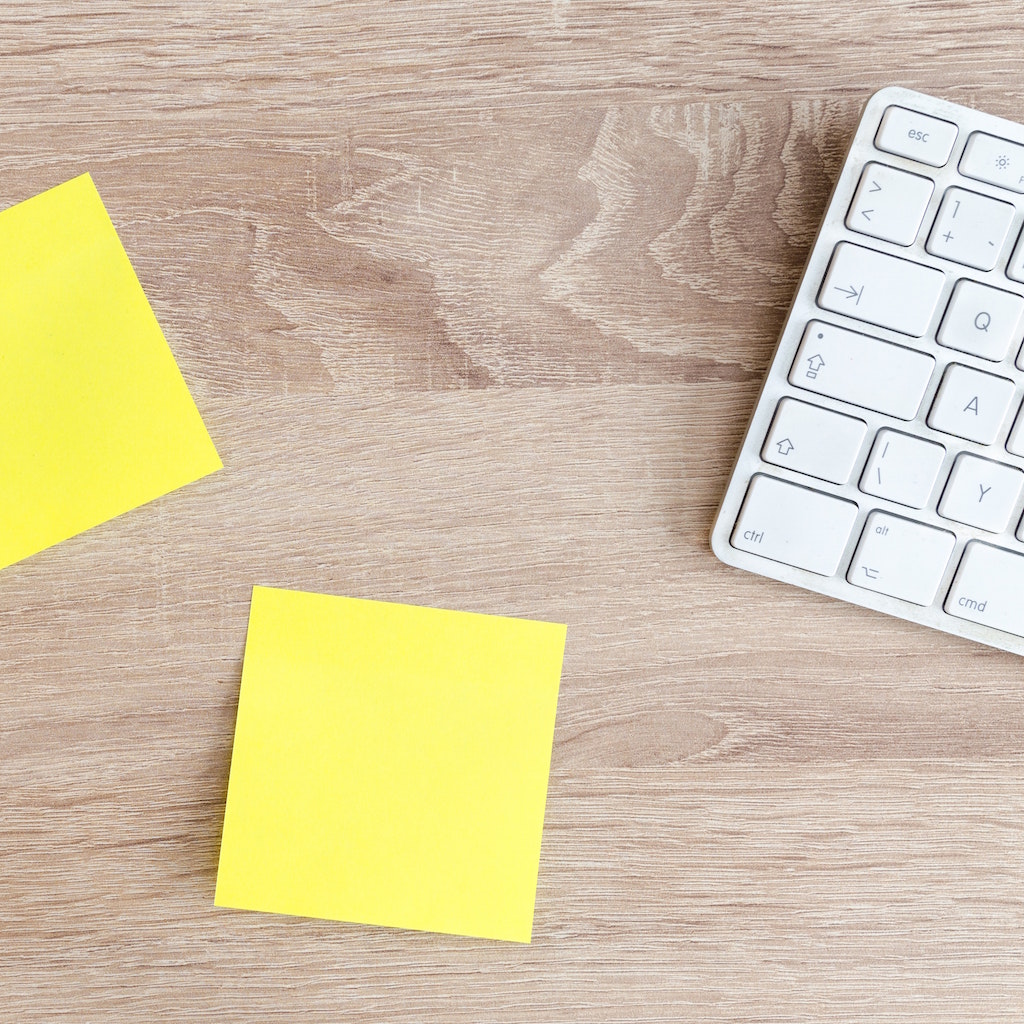Keyboard and yellow notes on a wooden desk
